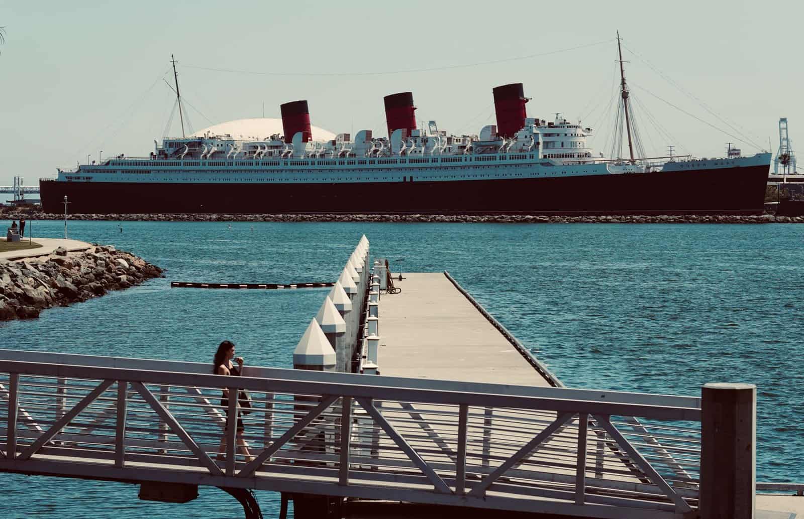 The iconic Queen Mary ocean liner docked at Long Beach, CA, with a scenic pier view.