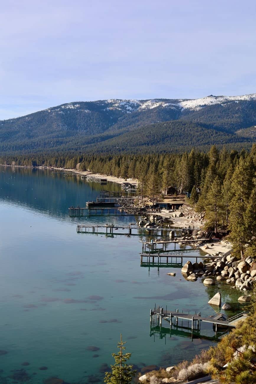 Stunning view of Lake Tahoe with pine trees, snowy mountains, and rustic piers.