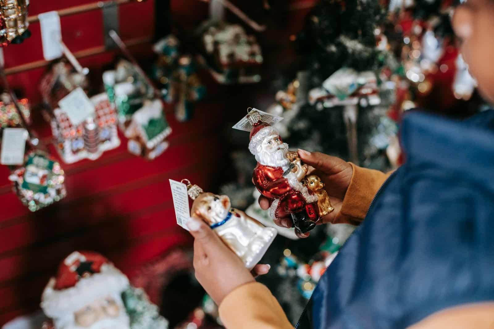 Side view of crop ethnic girl with Santa and dog toys standing in shop with Christmas decorations