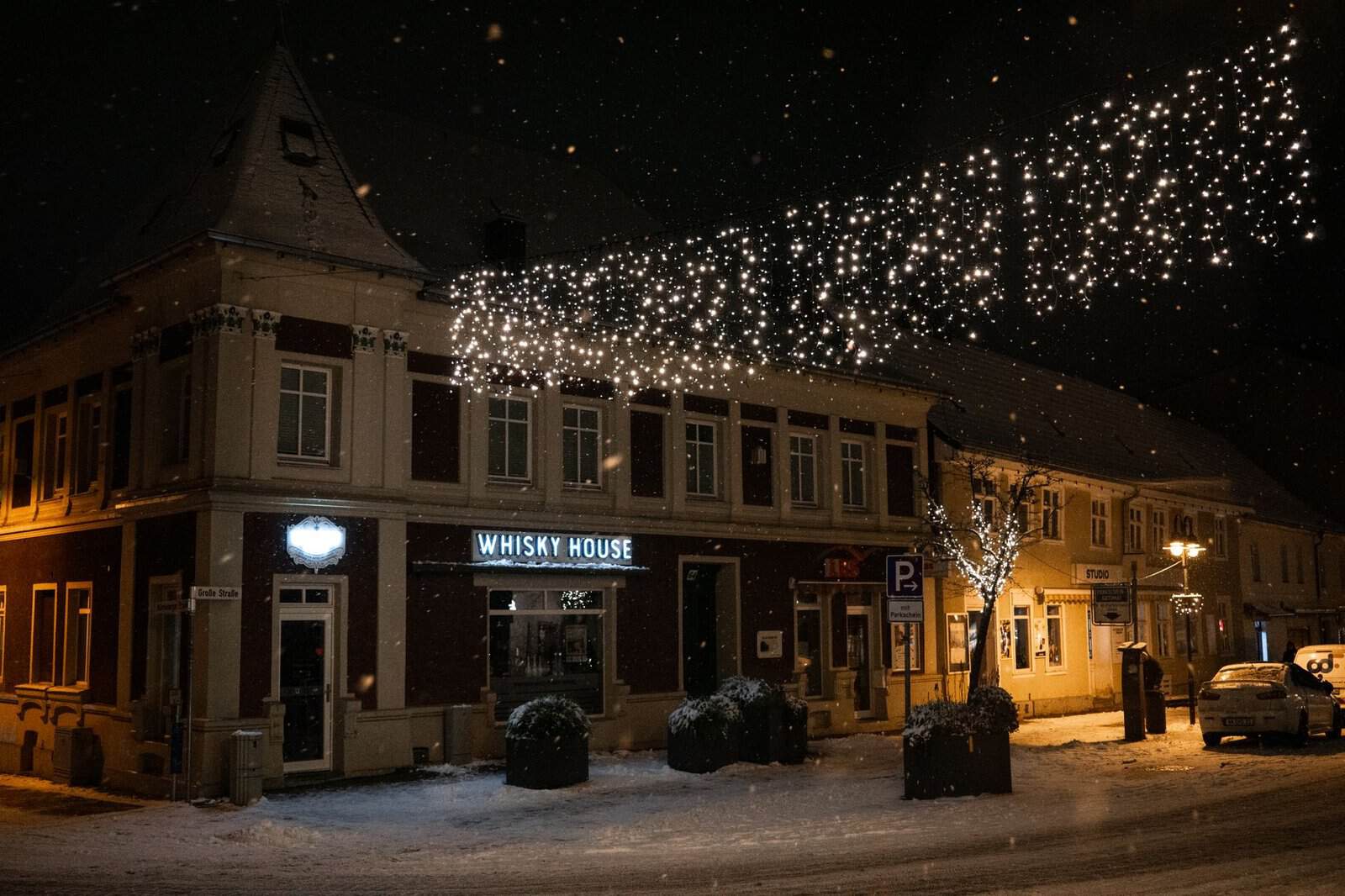 A cozy night scene of a snow-covered town with festive lights and a Whisky House building.