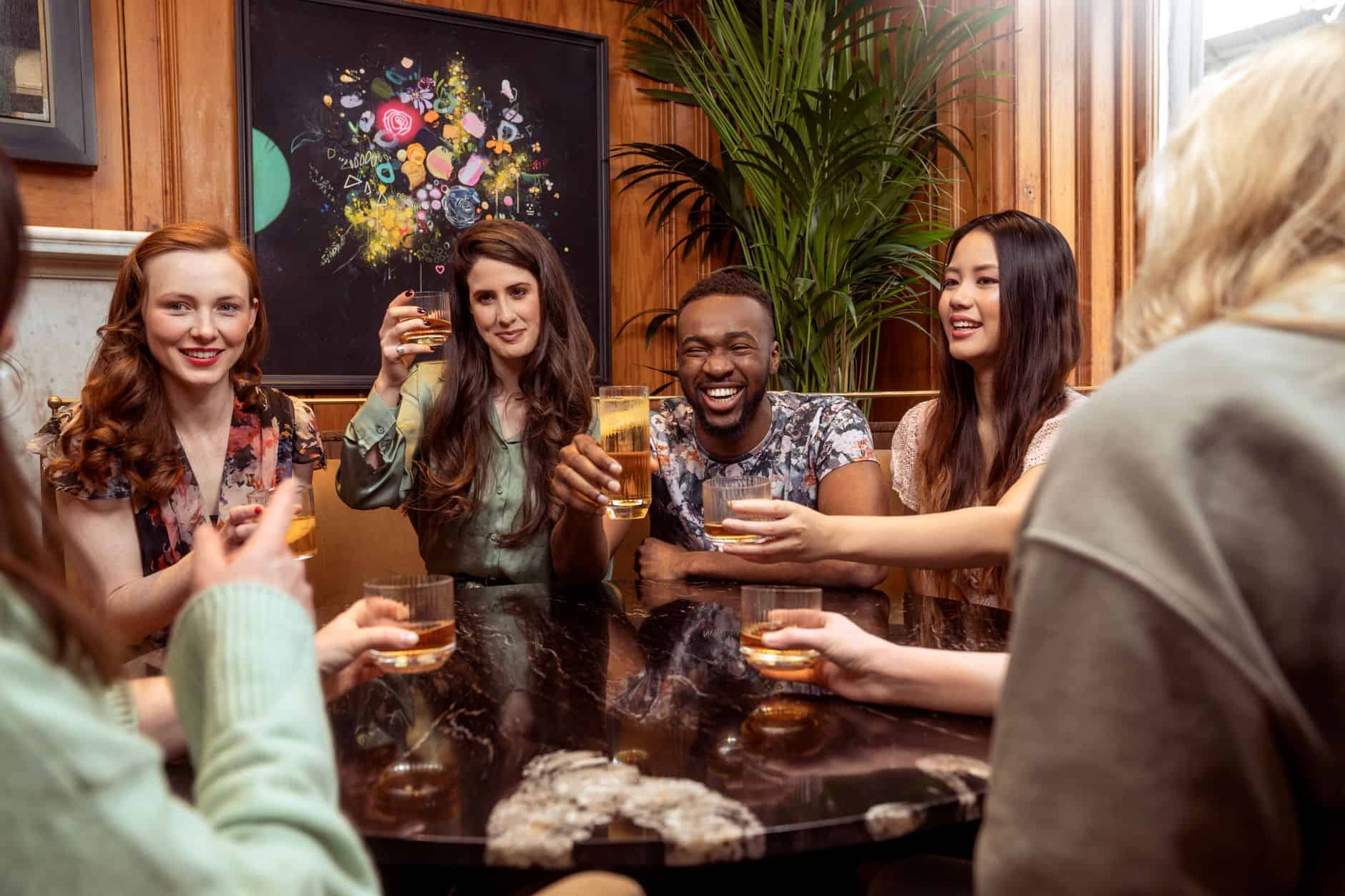 smiling friends sitting with drink by table